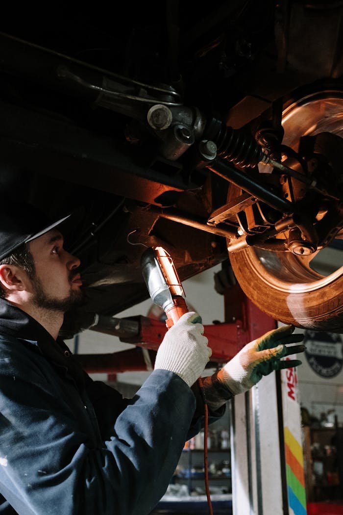 Home Mechanic uses a flashlight to inspect cars suspension in a garage setting.